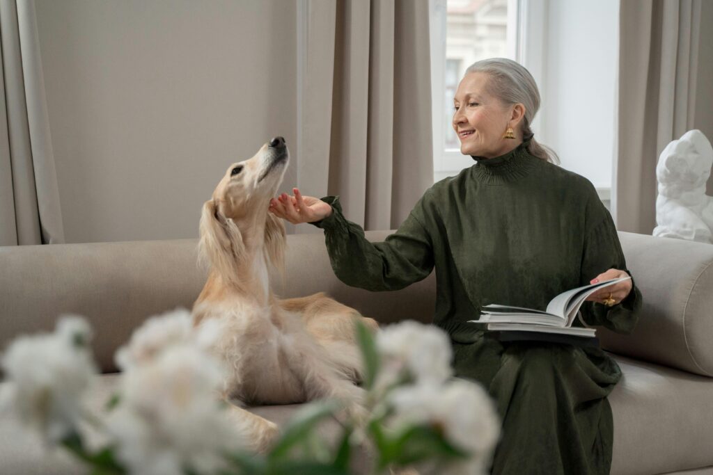 A senior woman in an elegant dress sits indoors with her Afghan Hound, enjoying a peaceful moment.